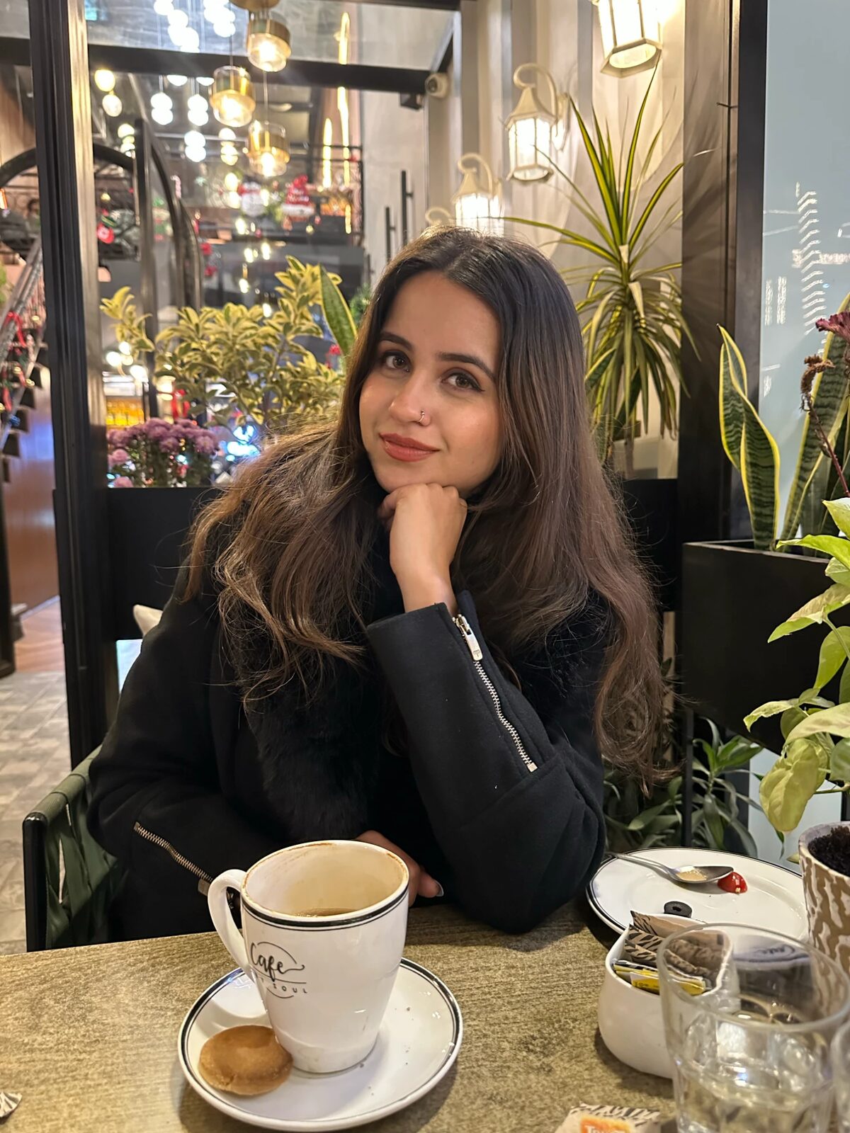 Angel Bhardwaj sitting at a café table, chin resting on her hand